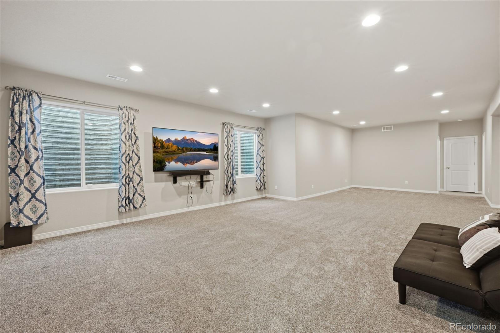 Carpeted living area with recessed lights, curtained windows, and a wall-mounted television.
