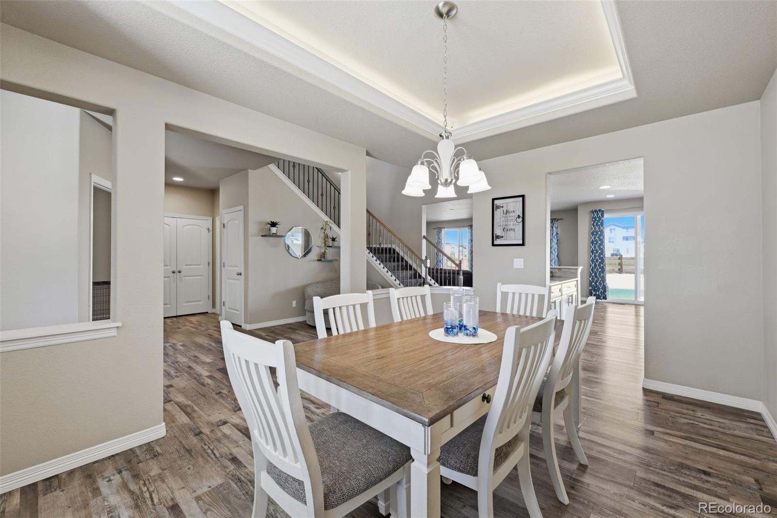 Dining room with a wooden table, white chairs, tray ceiling, and staircase.