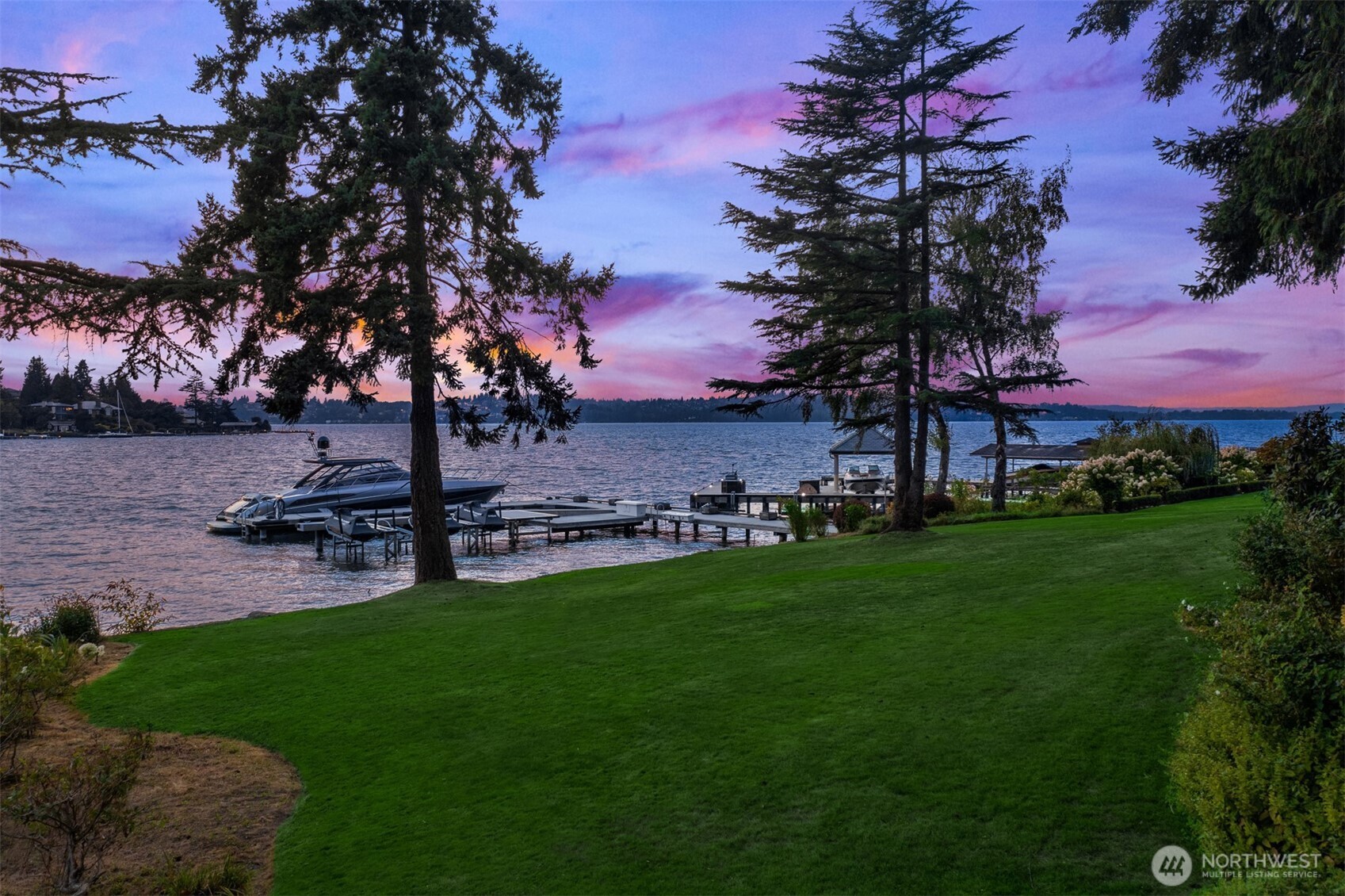 Waterfront lawn and private dock with a boat beneath a pink-purple dusk sky.
