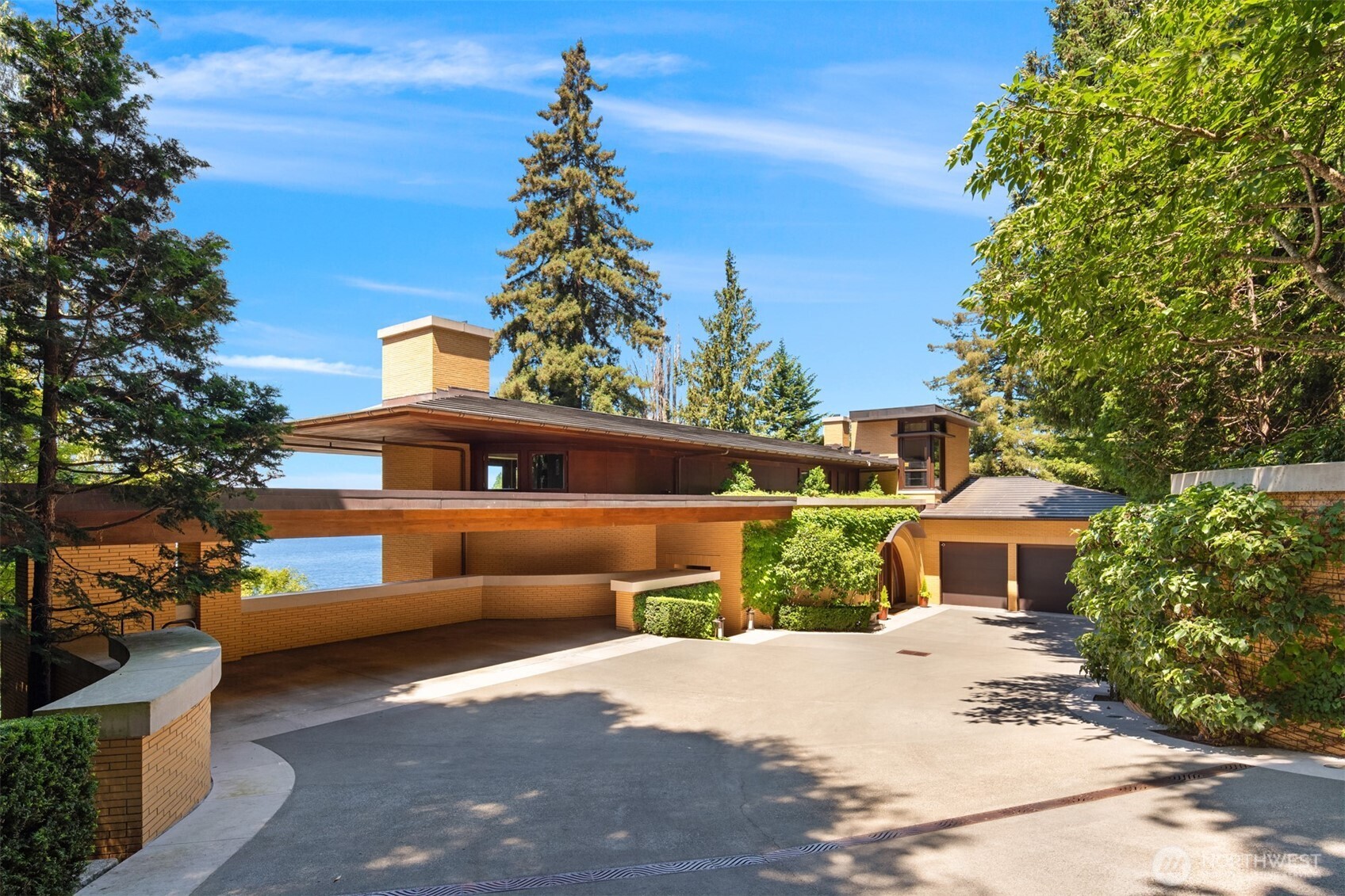 Modern brick home with broad flat roofs, a covered carport, and a glimpse of water beyond.