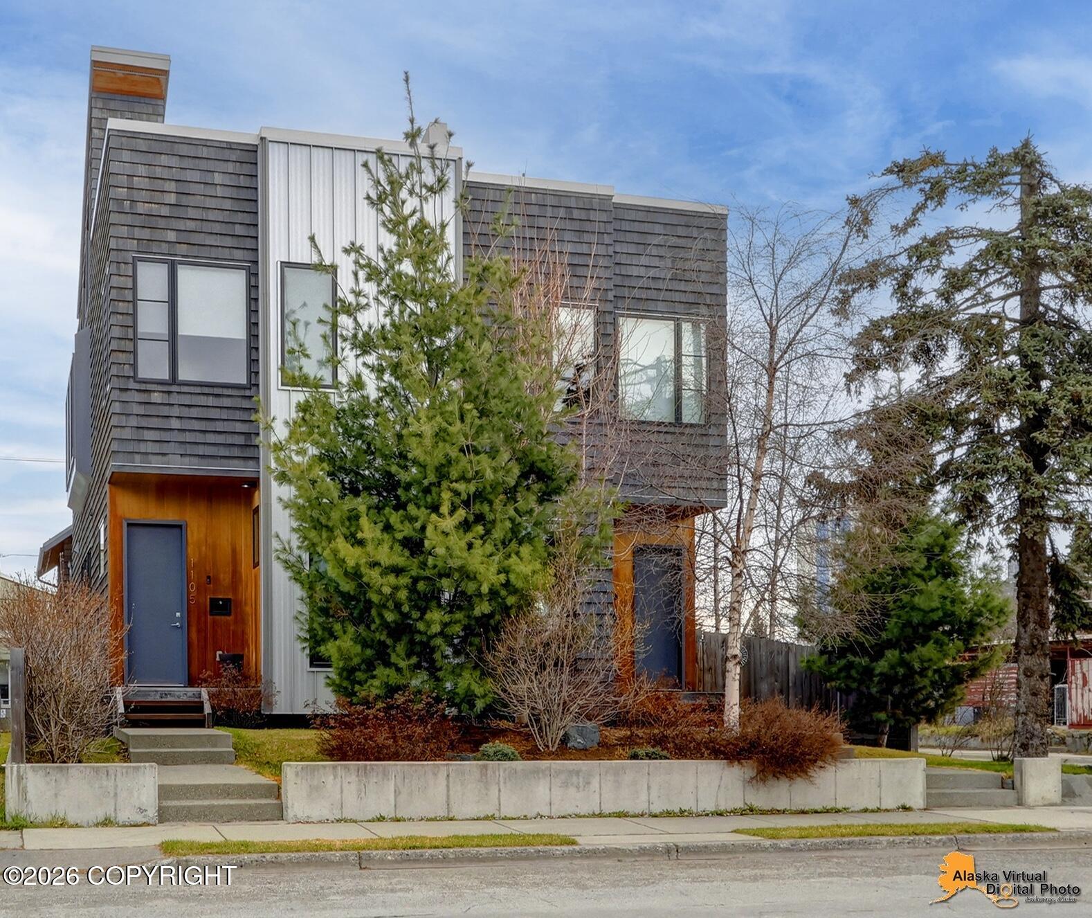 Modern multi-story Anchorage home with dark shingles, white panels, and warm wood entry surrounds.