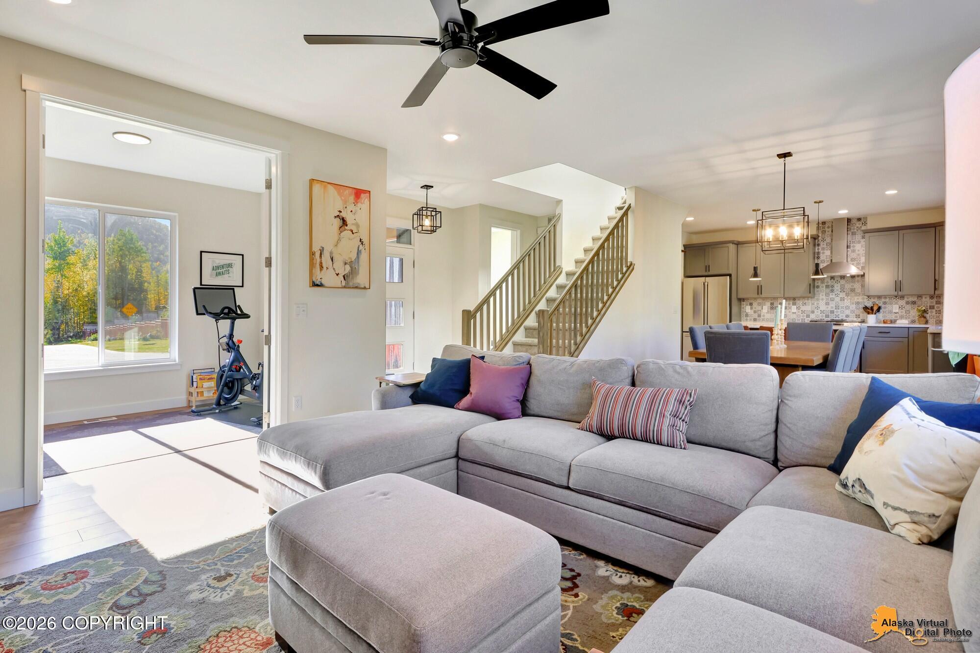 Open-plan living room with a gray sectional, staircase, and adjoining kitchen and dining area.