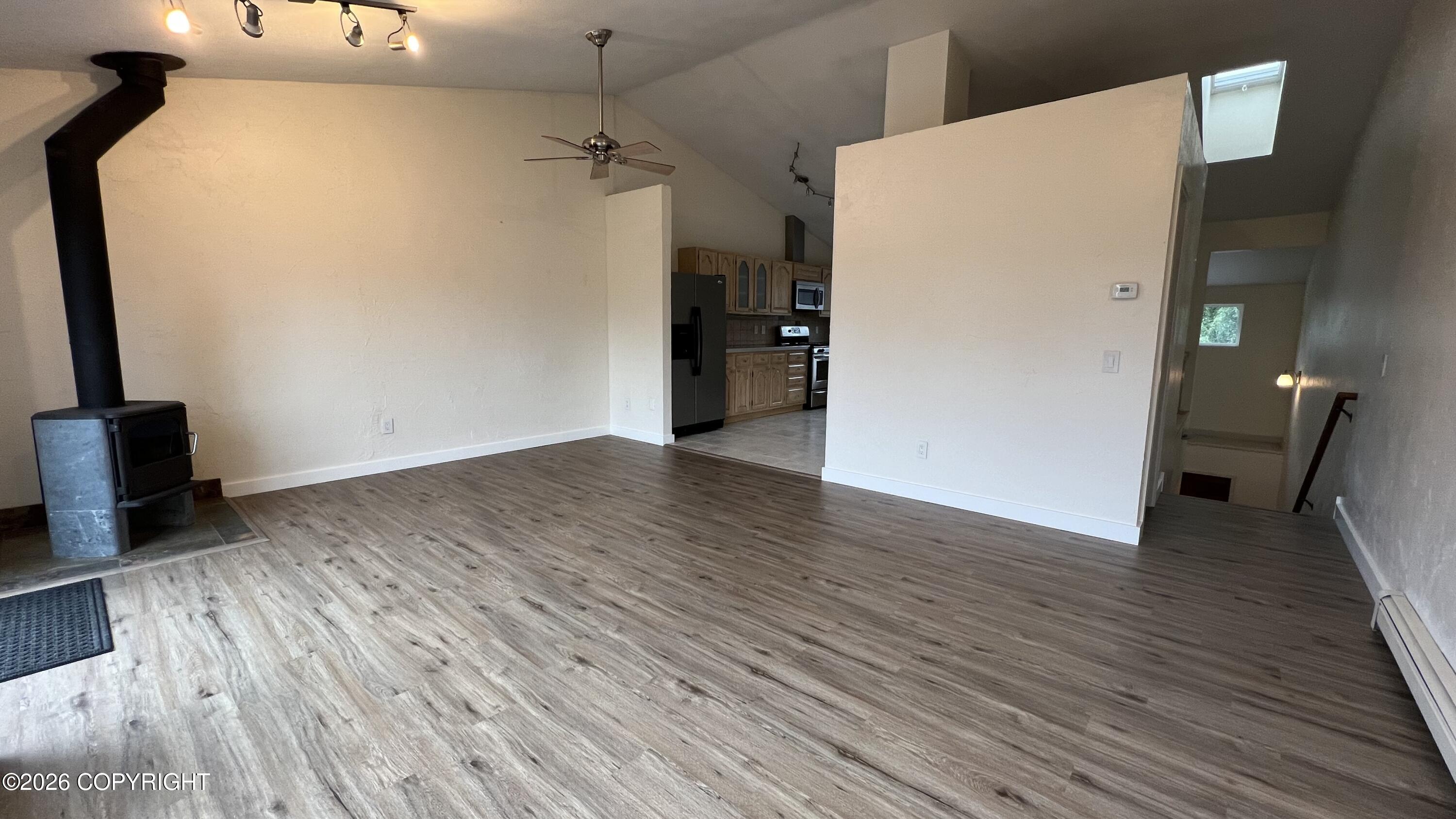Vacant living room with wood stove, gray plank flooring, and an open kitchen.