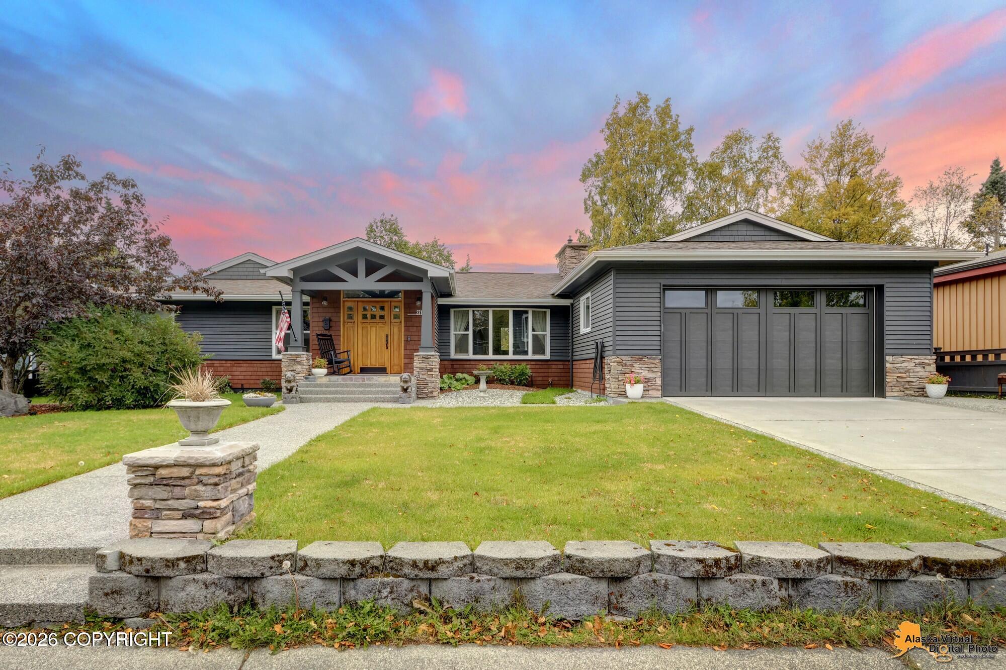 Gray single-story home with a large garage, covered entry, stone accents, and landscaped front lawn at sunset.
