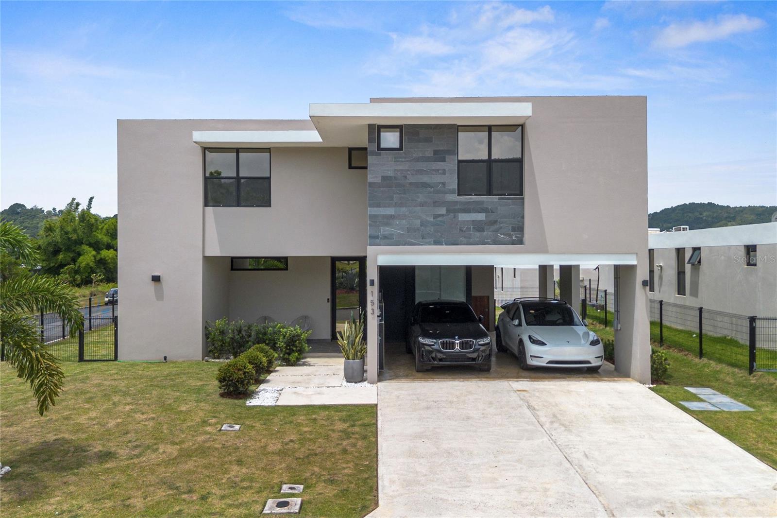 Modern two-story home with a dark stone facade, covered carport, and two cars in the driveway.
