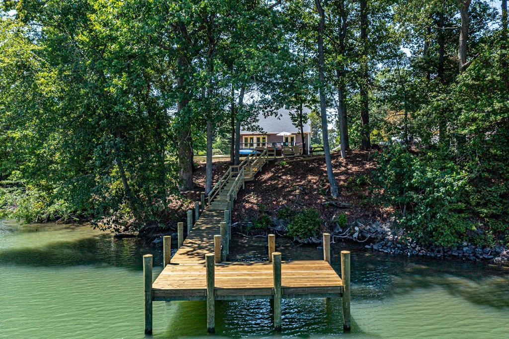 Wooden dock and walkway lead through a wooded shoreline to a waterfront home.
