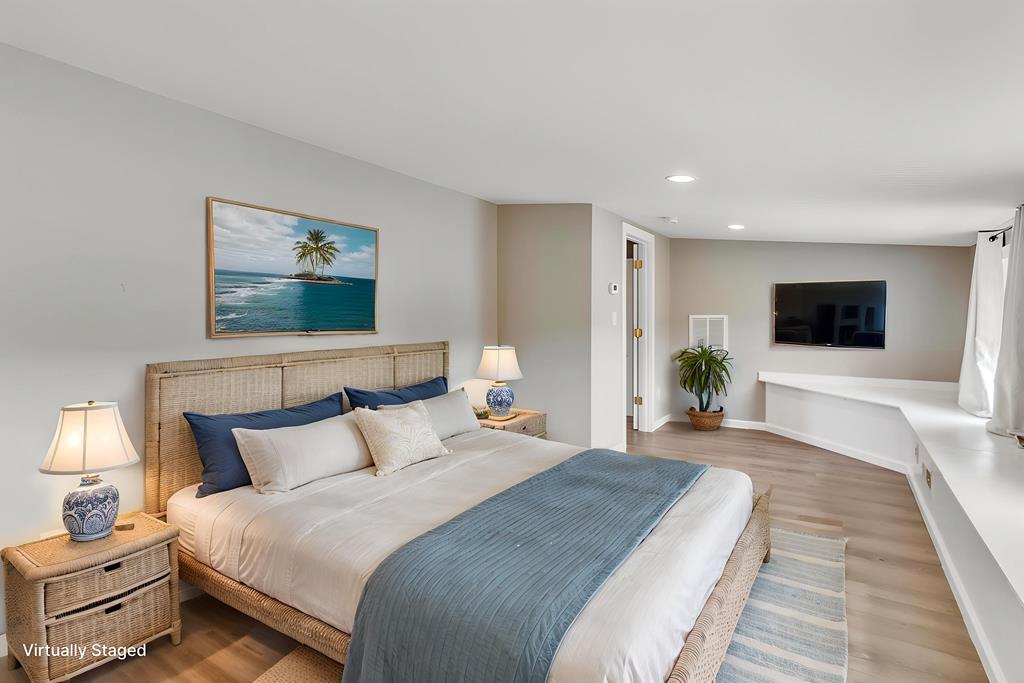 Virtually staged bedroom with a rattan-headboard bed, blue runner, tropical artwork, and wall-mounted TV.