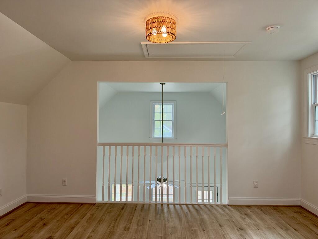 Upstairs landing with wood flooring, white railing, and a pendant light overlooking the foyer.