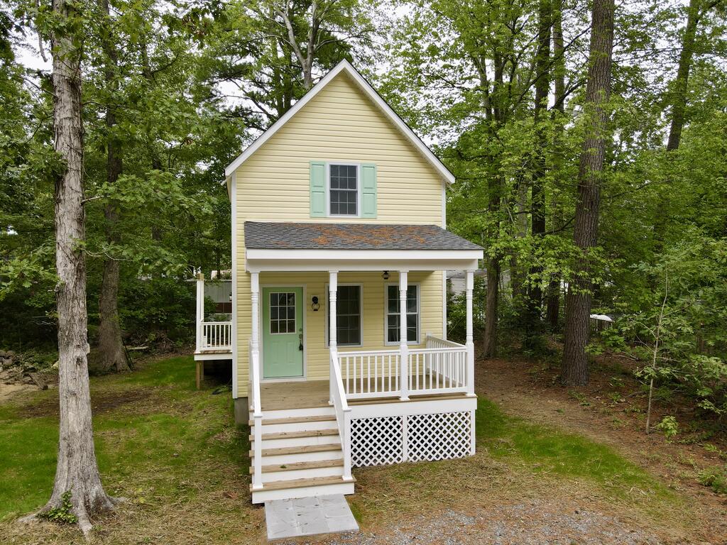 Yellow two-story cottage with mint-green shutters and door, white porch, surrounded by trees.
