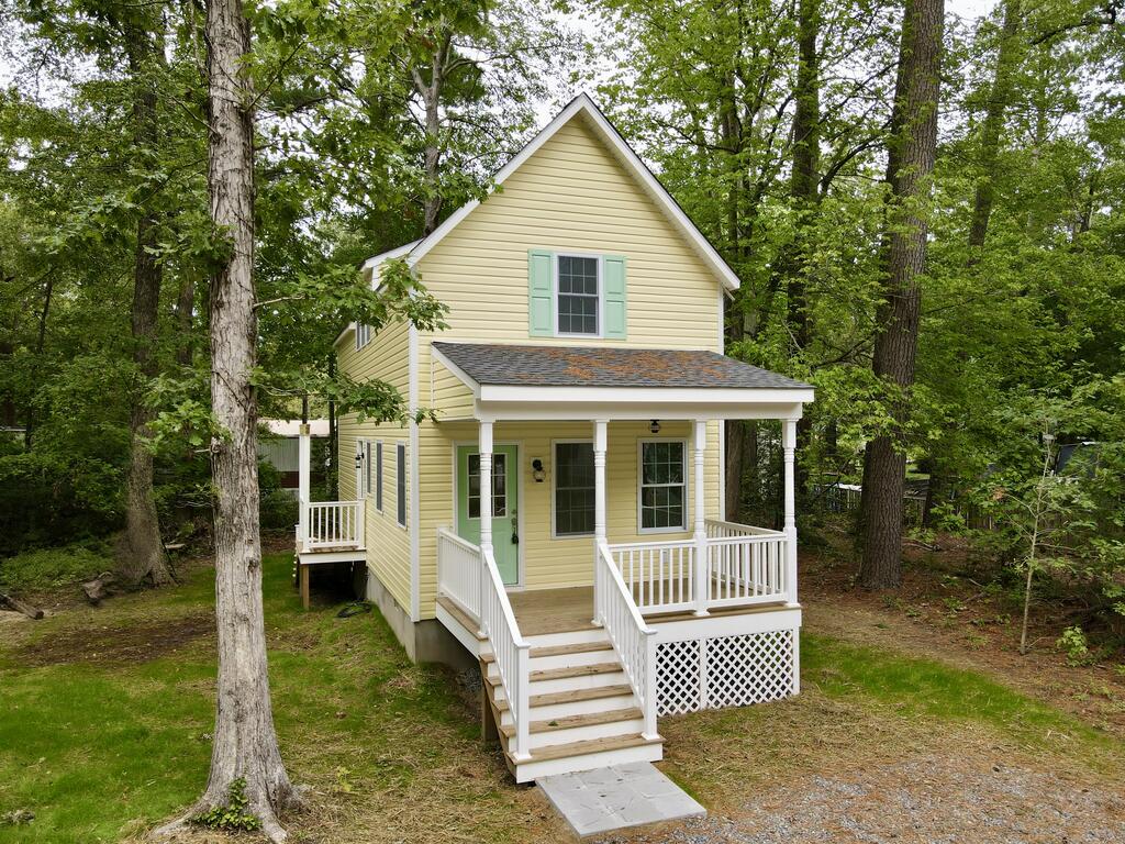 Pale-yellow two-story house with mint-green accents and a white-railed porch among trees.