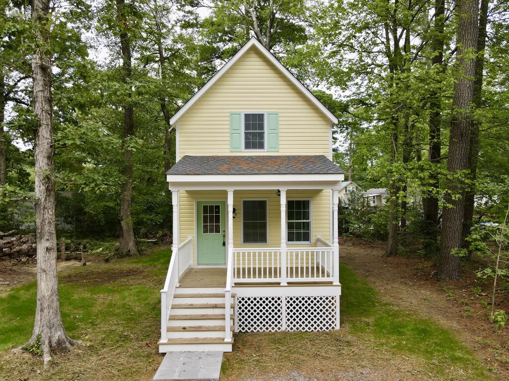 Pale yellow two-story house with a mint-green door and a white-railed front porch among mature trees.