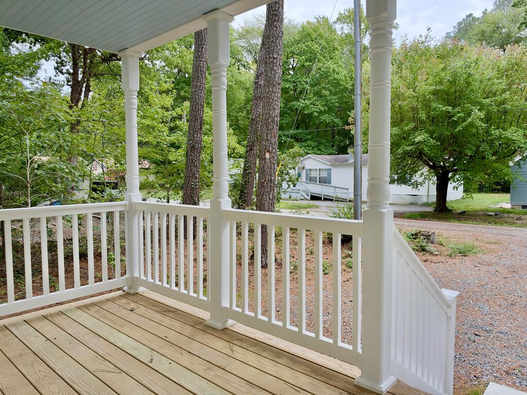 Covered wooden porch with white railings and columns overlooking a tree-lined gravel driveway.