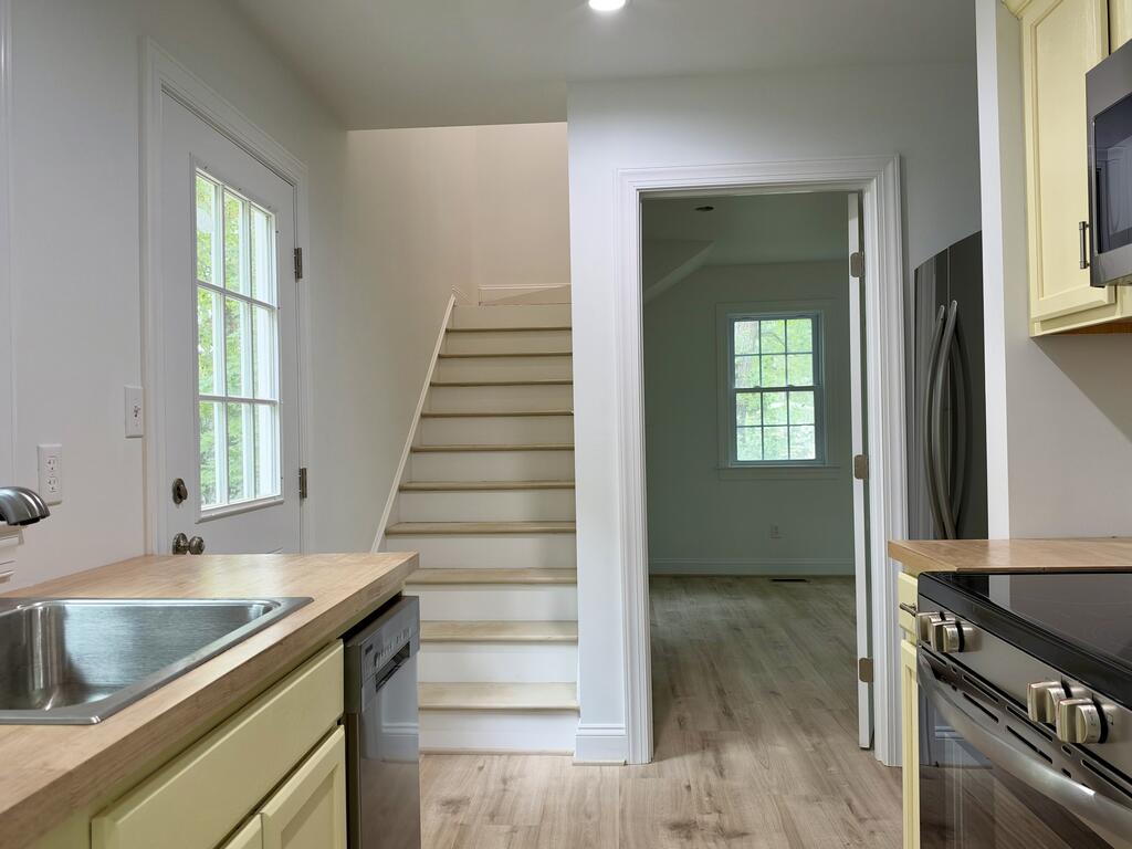 Kitchen with wood countertops and stainless appliances, beside a staircase and a glass-paneled door.