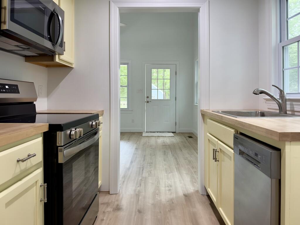 Kitchen with pale yellow cabinets and wood counters, looking toward a bright entryway.