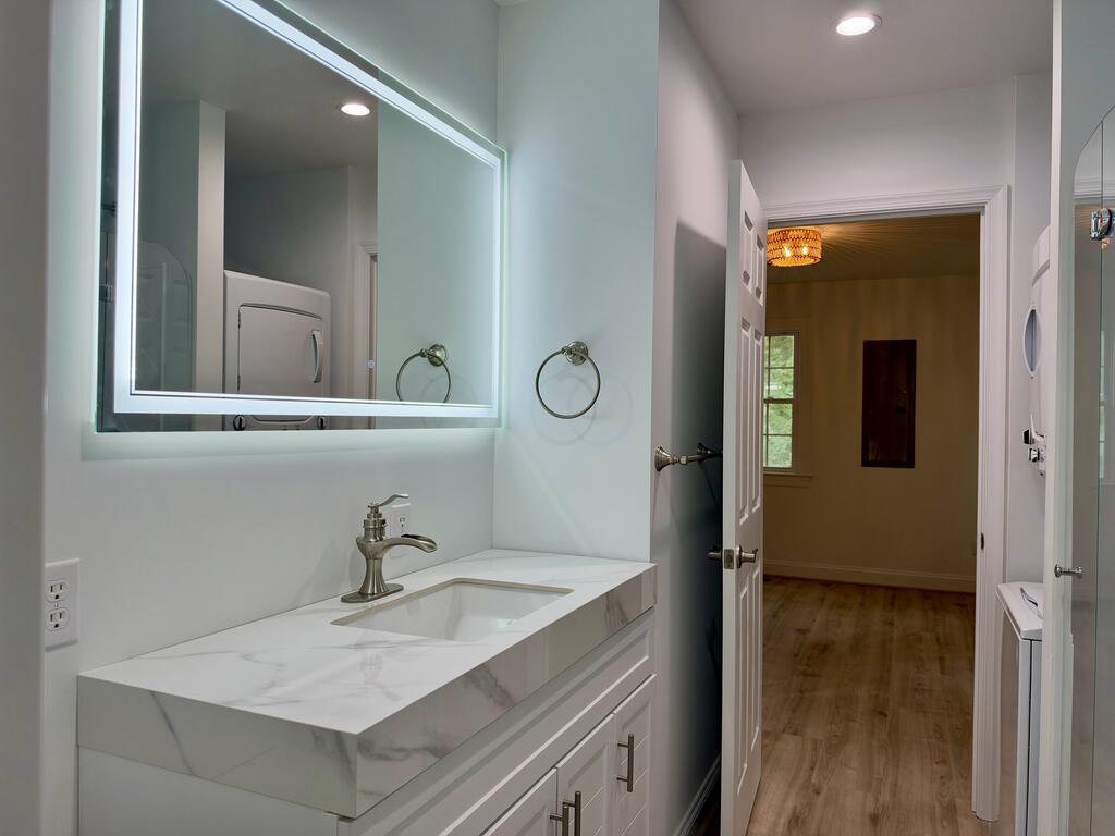 Bathroom vanity with a marble-look countertop and large mirror beside an open doorway.