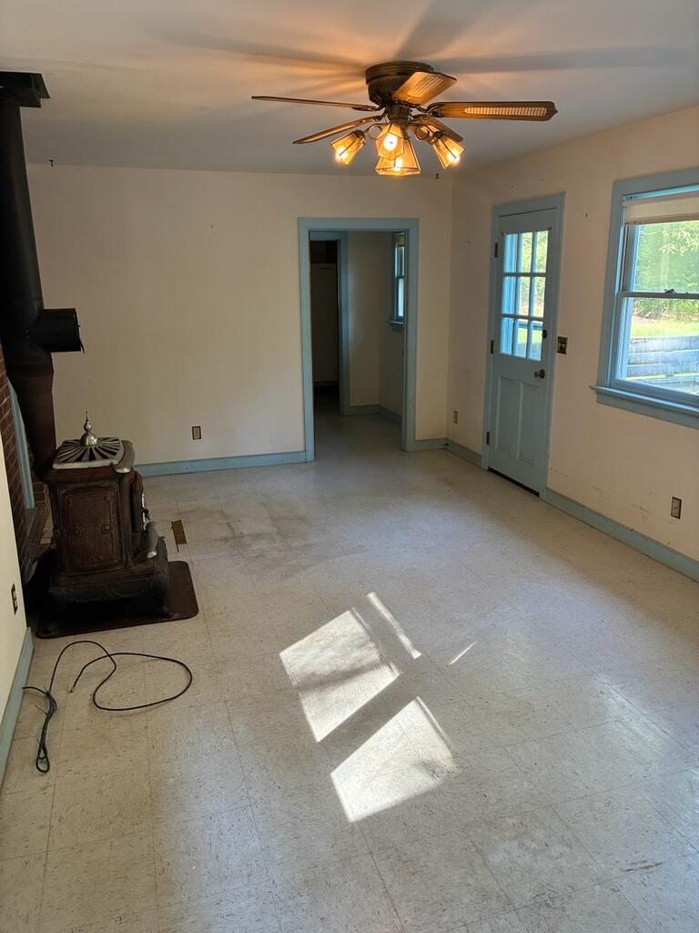 Mostly empty room with a black wood stove, ceiling fan, and blue-trimmed door and windows.