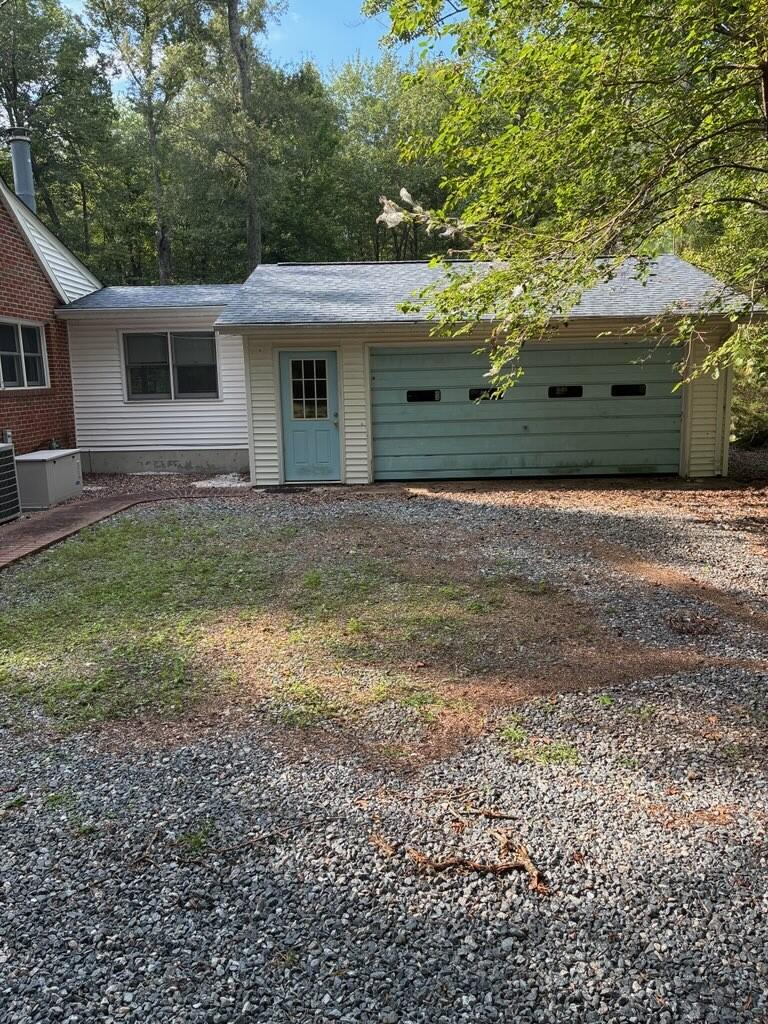 Home exterior with a pale green garage door, blue entry door, and gravel driveway.