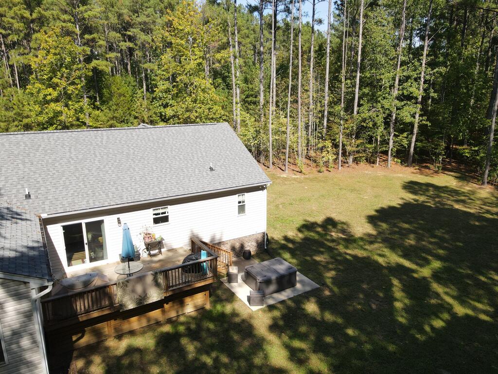 Rear of a house with a broad deck and hot tub beside a wooded yard.