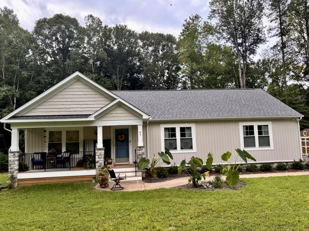 Single-story home with a covered porch, stone columns, and wooded backdrop.