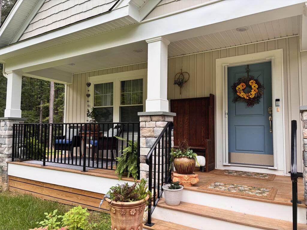 Covered front porch with a blue wreath-adorned door, stone column bases, black railings, and potted plants.