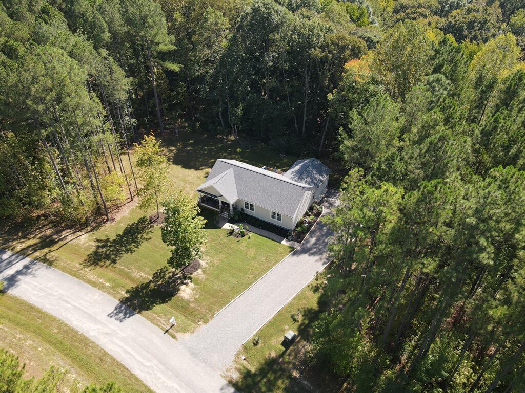 Aerial view of a single-story home on a wooded lot with a long driveway.
