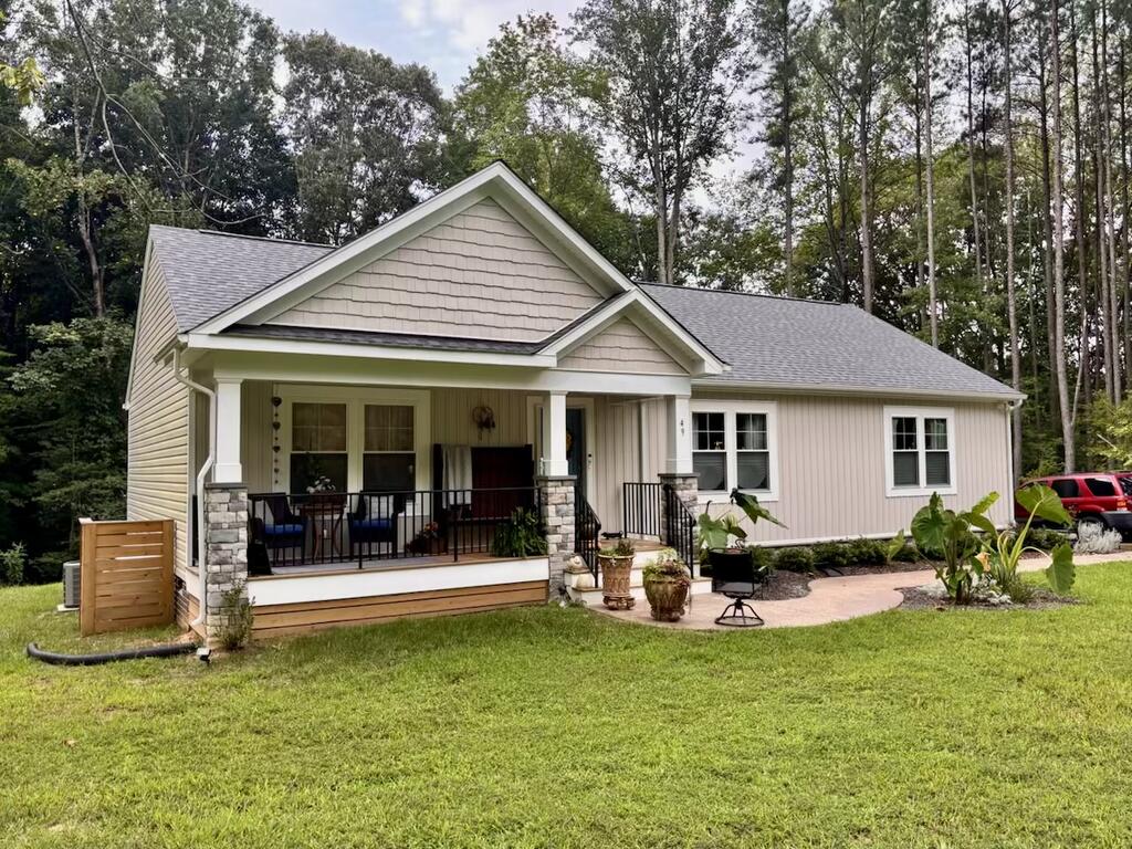 Light-colored home with a stone-columned front porch, broad lawn, and wooded backdrop.