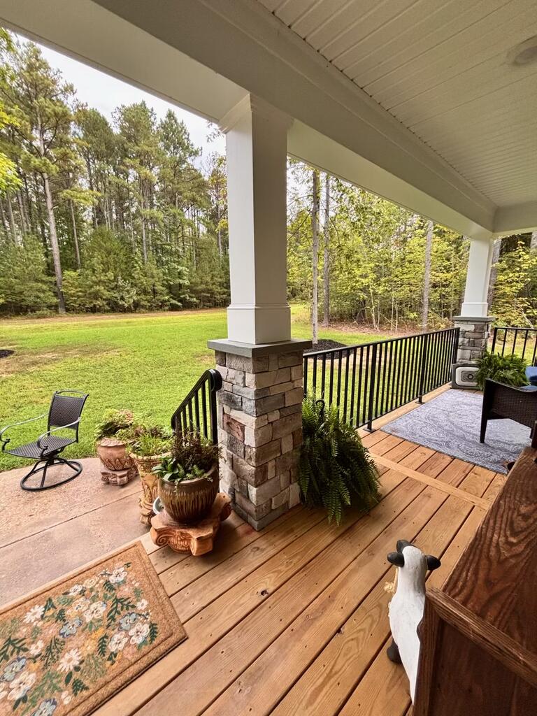 Covered wooden porch with stone columns, black railing, and a wooded lawn view.