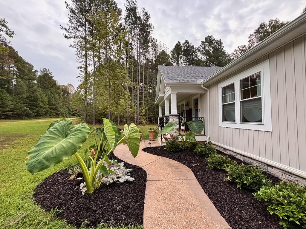 Home with a covered porch, curved garden path, broad lawn, and mature trees.