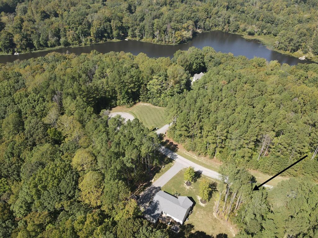 Aerial view of a wooded property with a house, cleared lawn, and water beyond the trees.