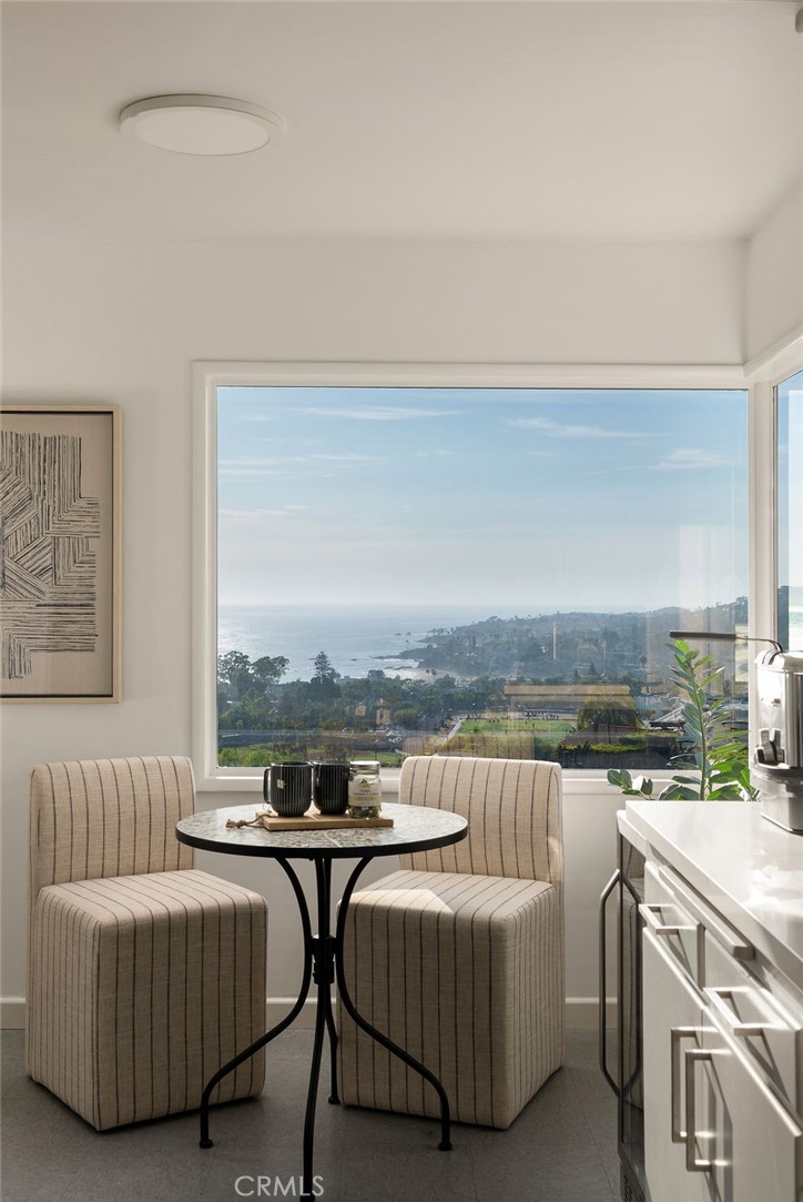Breakfast nook with striped chairs and a round table overlooking the ocean through a large window.
