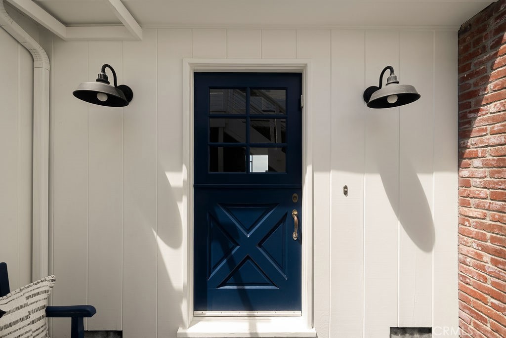 Home entrance with a navy blue paneled door, black sconces, white siding, and a red brick edge.