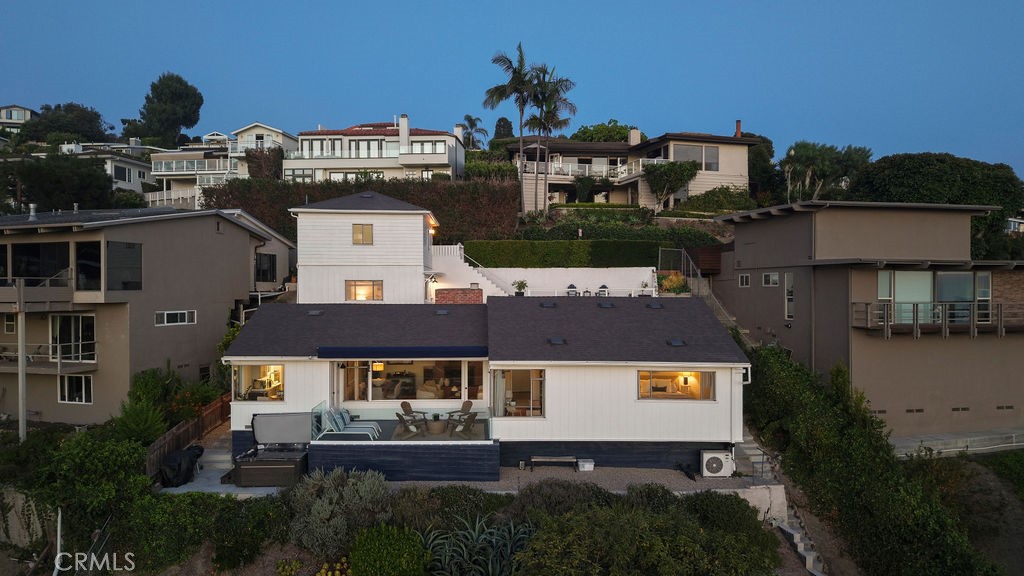 White coastal home's rear exterior and furnished patio viewed from above at dusk.