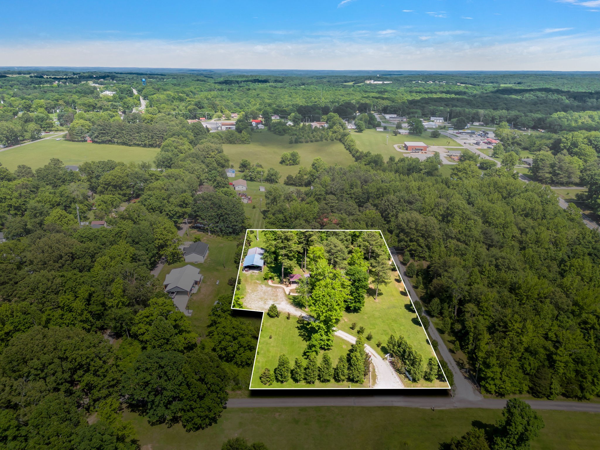 Aerial view of a wooded property outlined in white, with a curved driveway, open lawn, and buildings partly screened by trees.