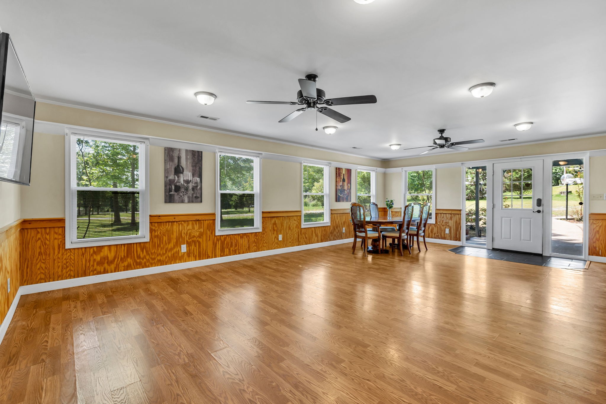 Dining room with hardwood floors, wood-paneled walls, multiple windows, and ceiling fans.