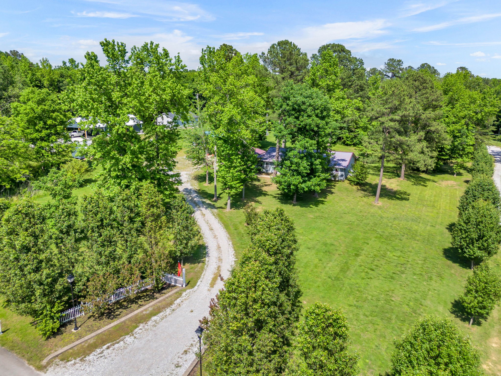 Aerial view of a house surrounded by mature trees, with a broad lawn and curving gravel driveway.