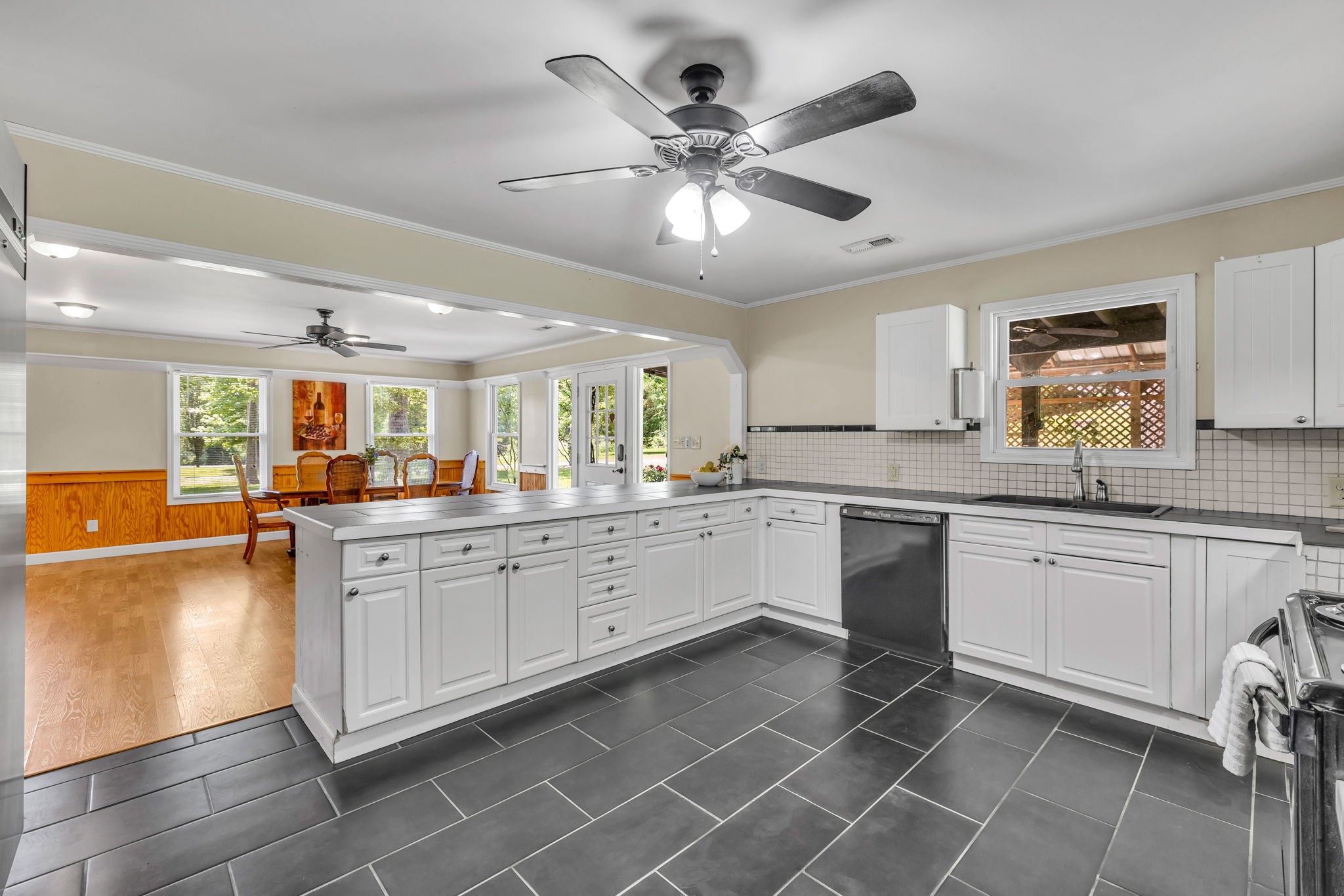 Kitchen with white cabinetry, a wide island, dark tile floors, and an adjoining dining area.