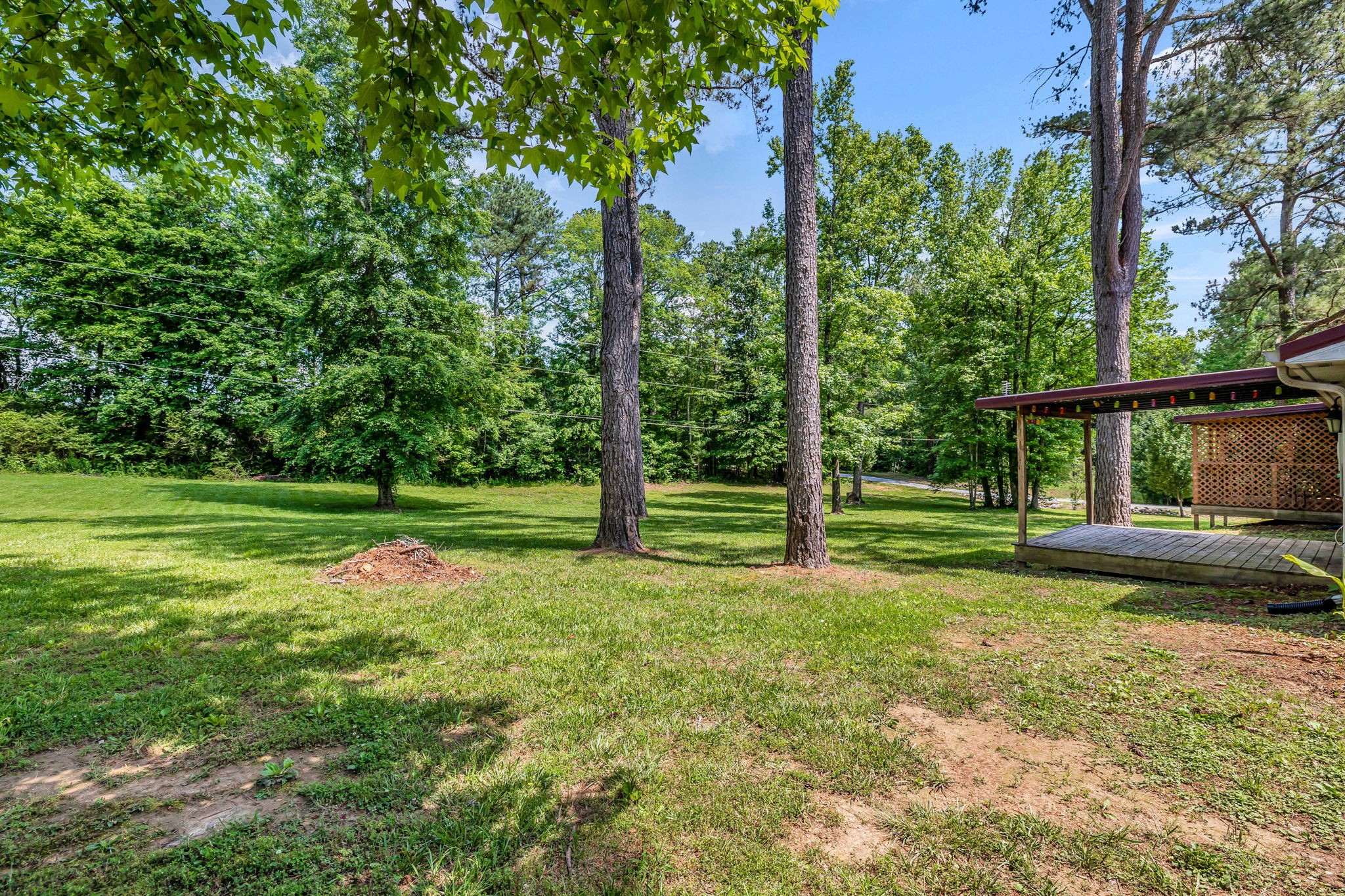 Backyard lawn shaded by mature trees, with a raised wooden deck beside the house.