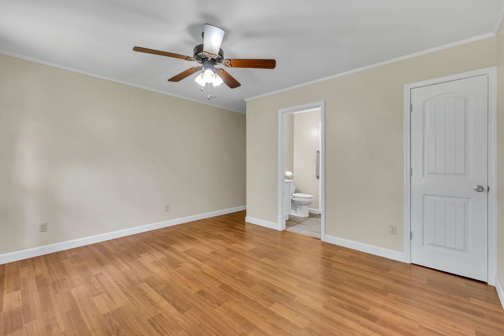 Empty room with wood flooring and ceiling fan, opening to a bathroom.