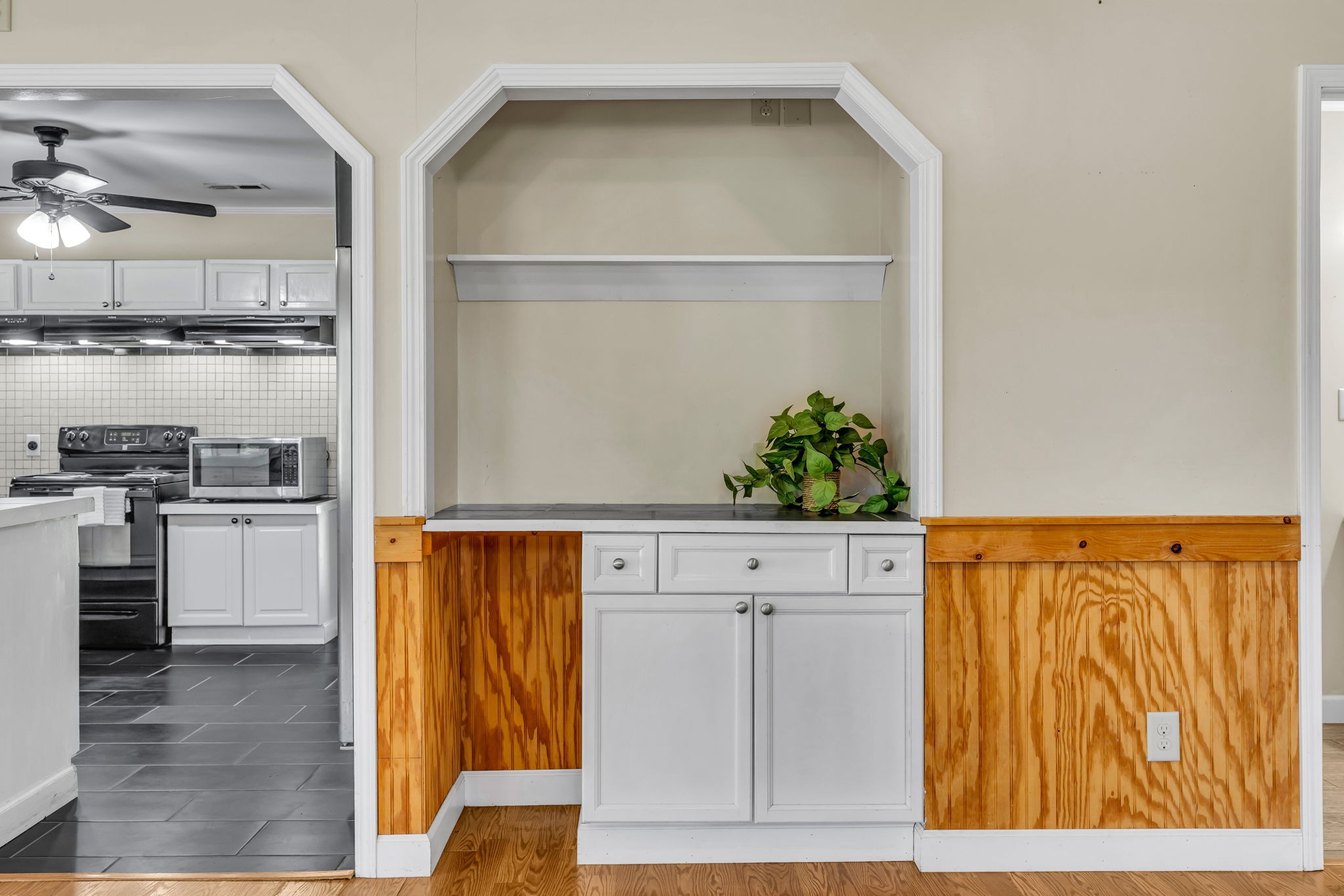 Kitchen with white cabinetry, stainless appliances, and a built-in cabinet against wood-paneled walls.
