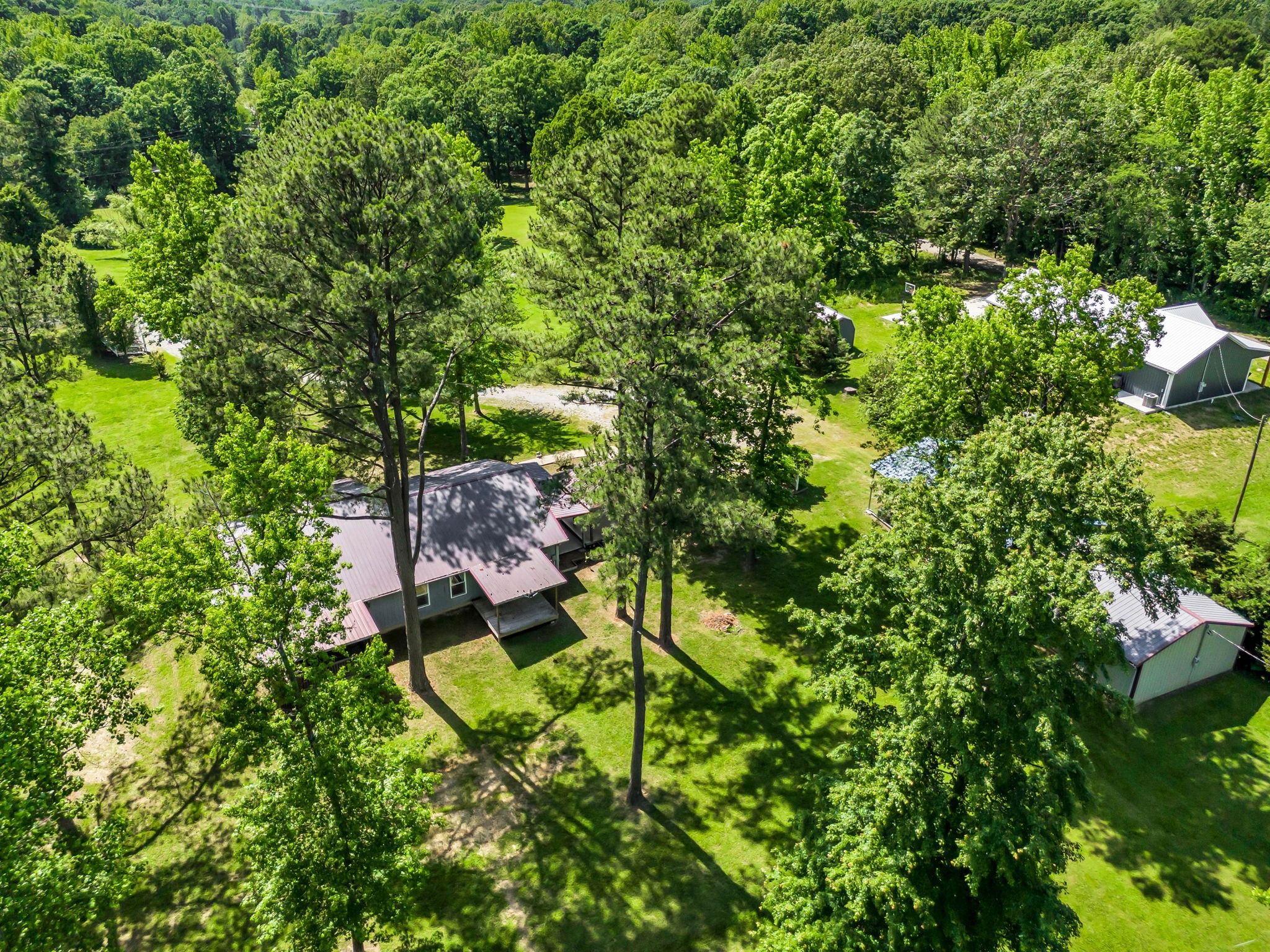 Aerial view of a home and outbuildings among mature trees and open lawn.