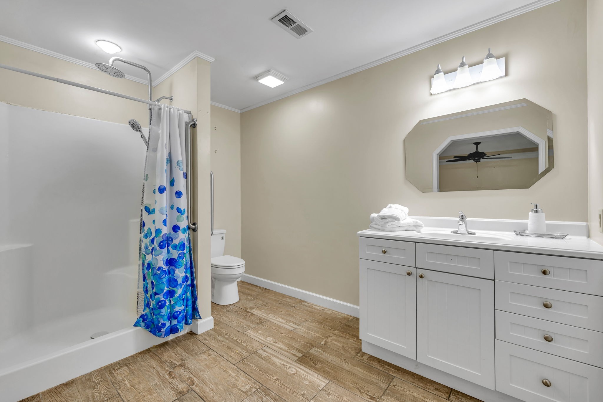 Bathroom with a blue floral shower curtain, white vanity, and wood-look tile floor.
