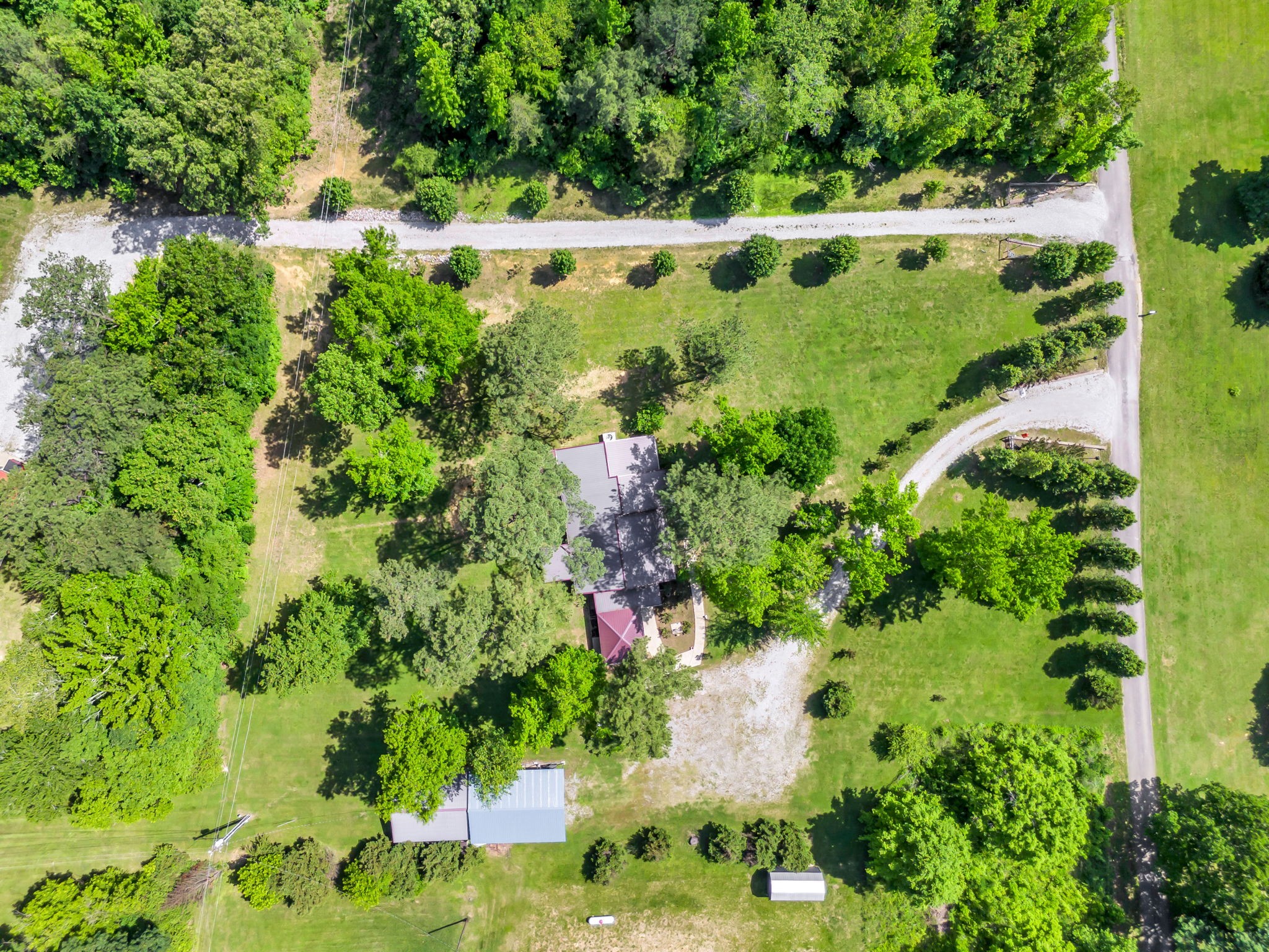 Aerial view of a tree-shaded home, broad lawn, gravel drives, and outbuildings.
