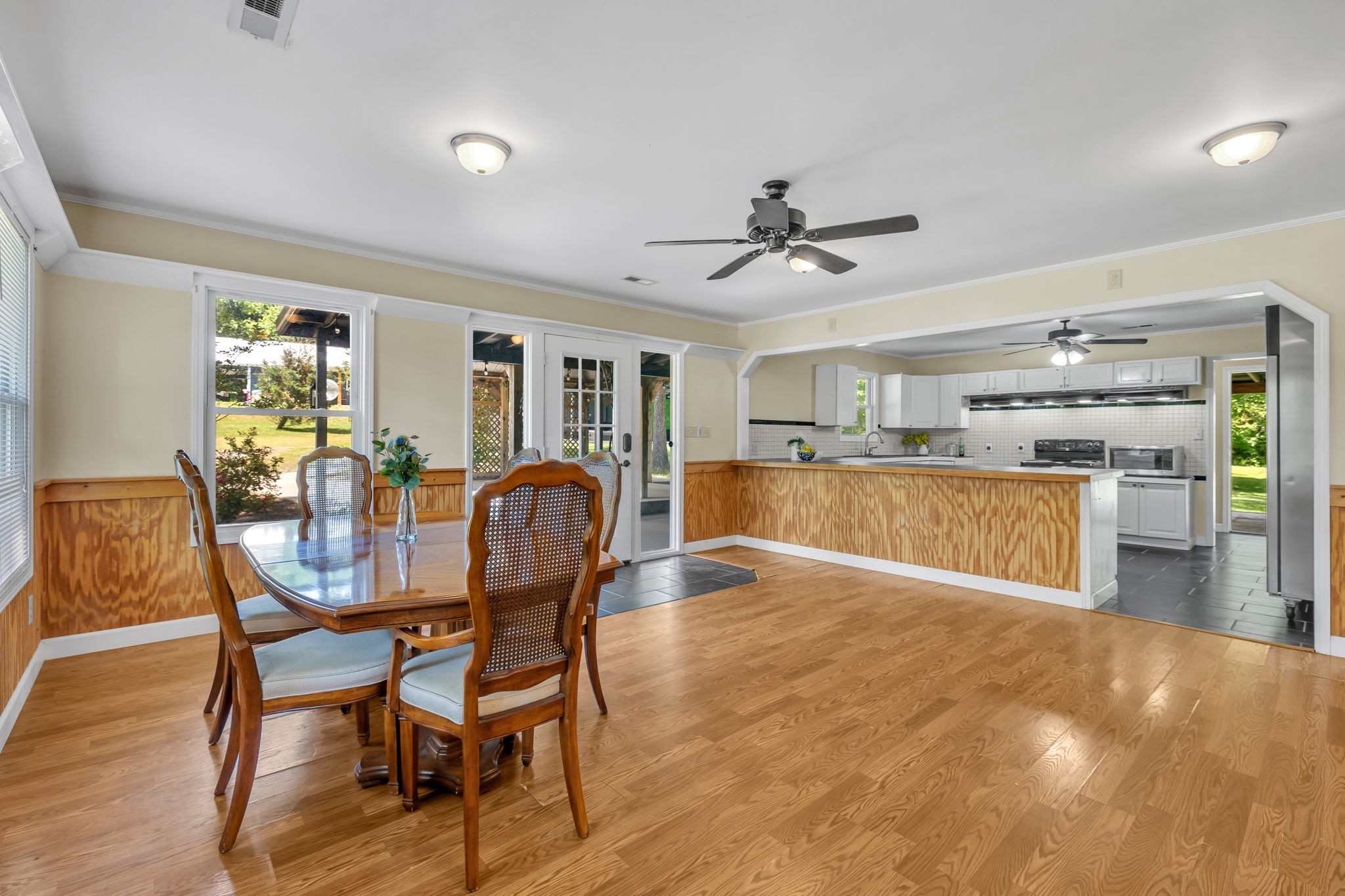 Dining room with a wooden table opening into a kitchen with white cabinets and a long peninsula.