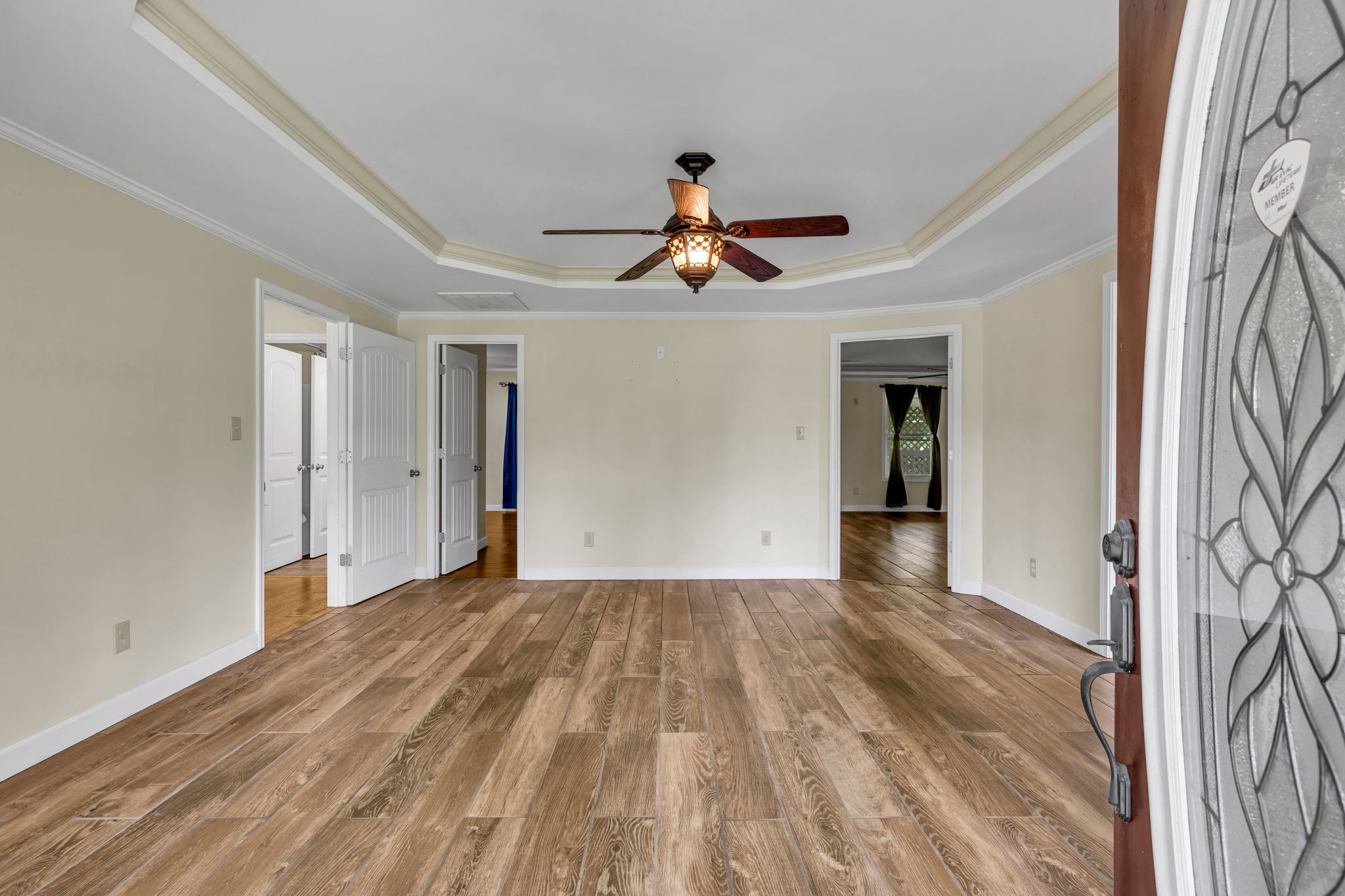 Empty living room with wood-look flooring, a tray ceiling, and a lit ceiling fan, viewed from the front door.