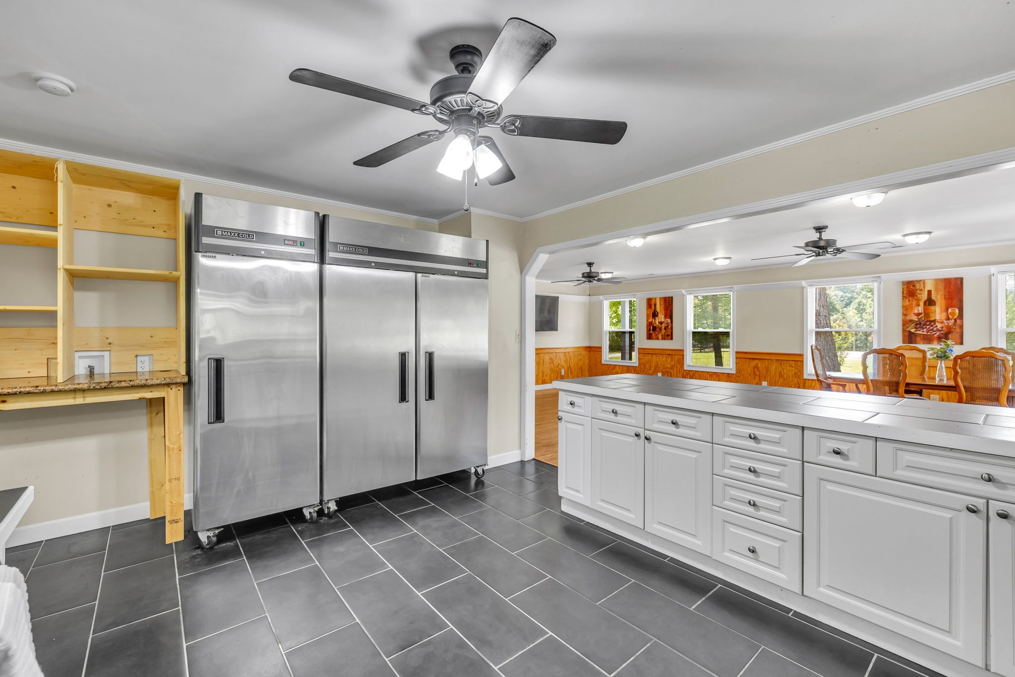 Kitchen with two stainless steel refrigerators, a long white storage island, and an adjoining dining area.