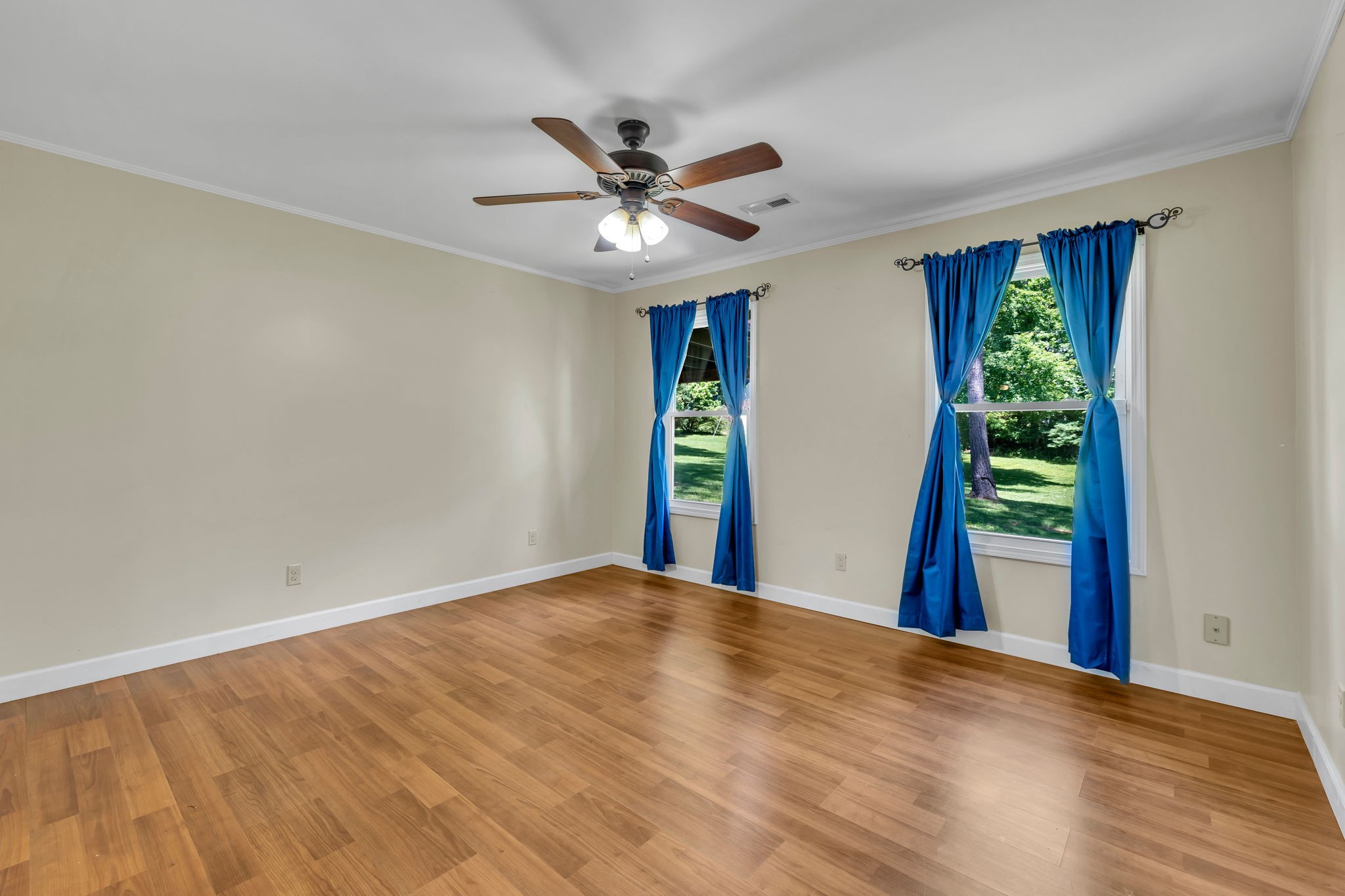 Empty bedroom with wood floors, blue curtains, and a ceiling fan.
