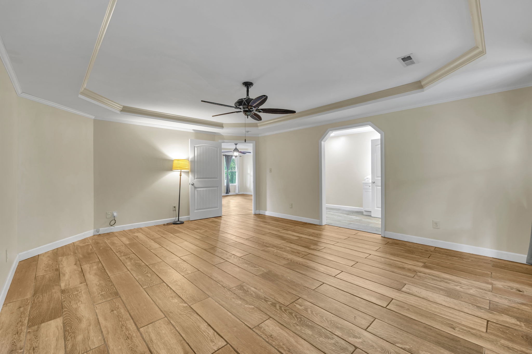 Empty room with wood-look plank flooring, a tray ceiling, ceiling fan, and open doorways.