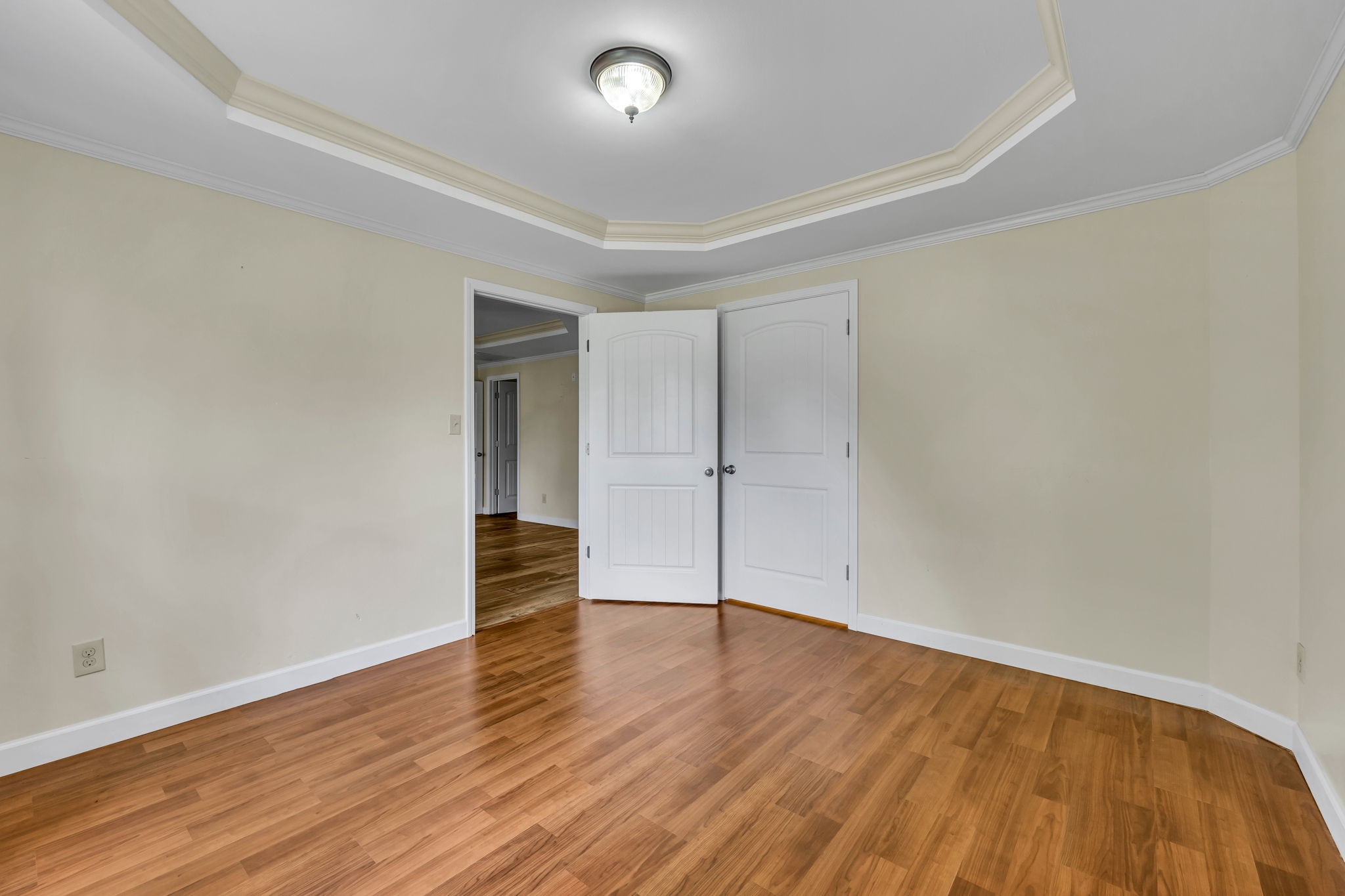 Empty room with wood floors and a tray ceiling beside two white paneled doors.