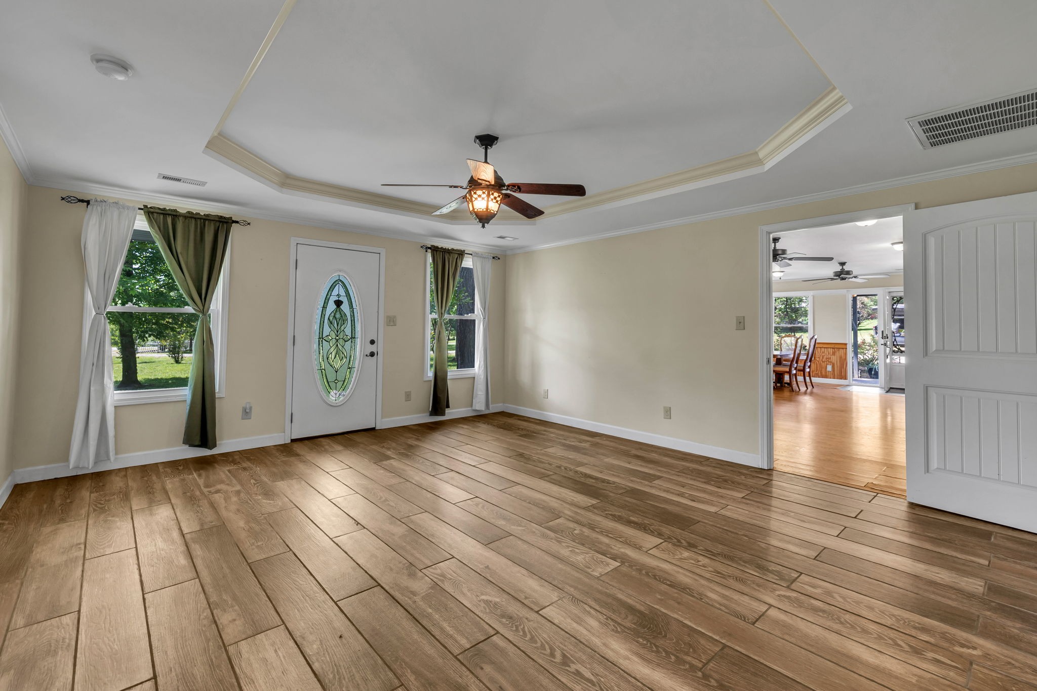 Empty front room with wood-look tile flooring, tray ceiling, and a glass-paneled front door.