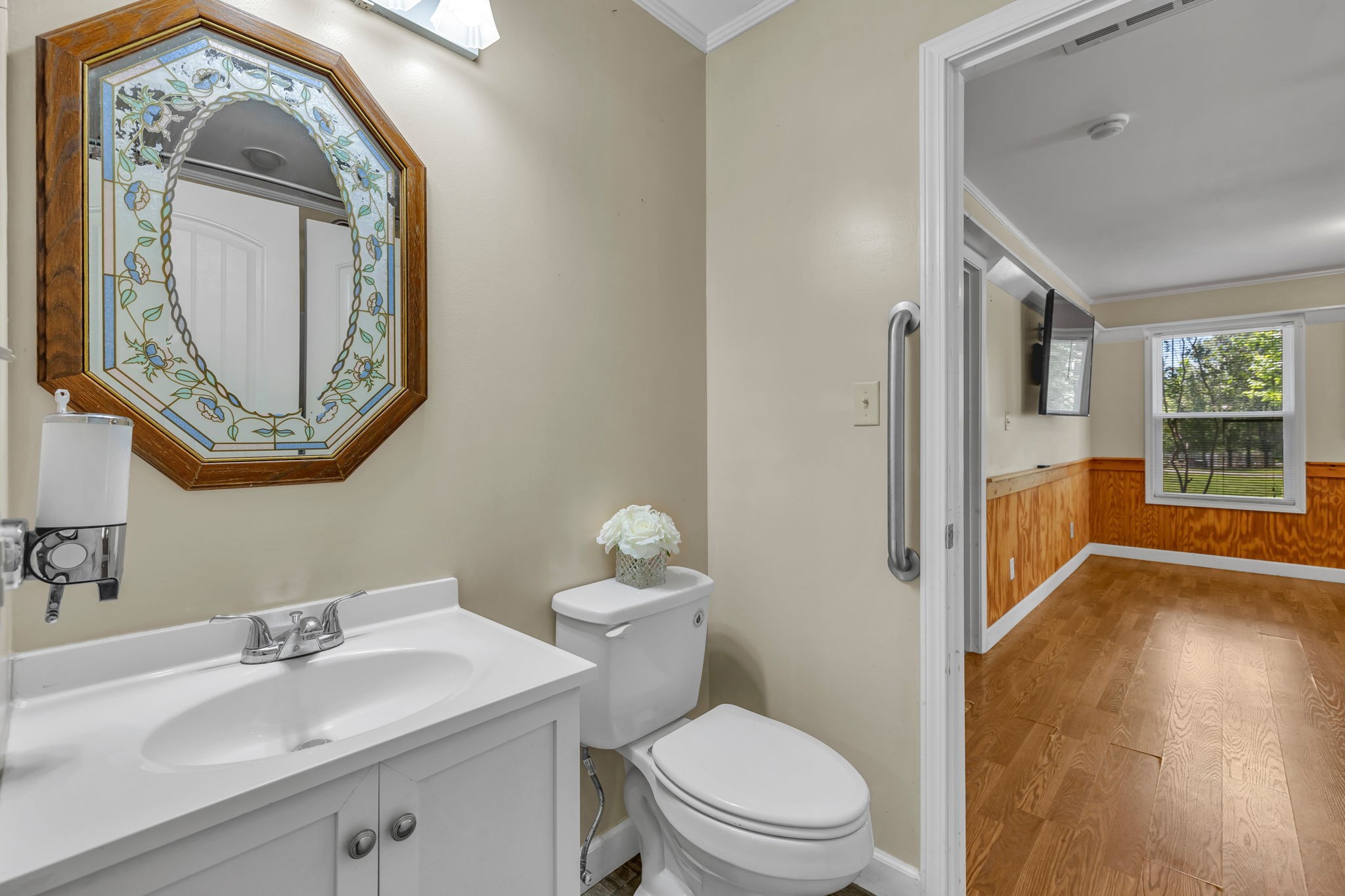 Bathroom with an ornate octagonal mirror and doorway to a wood-paneled room.